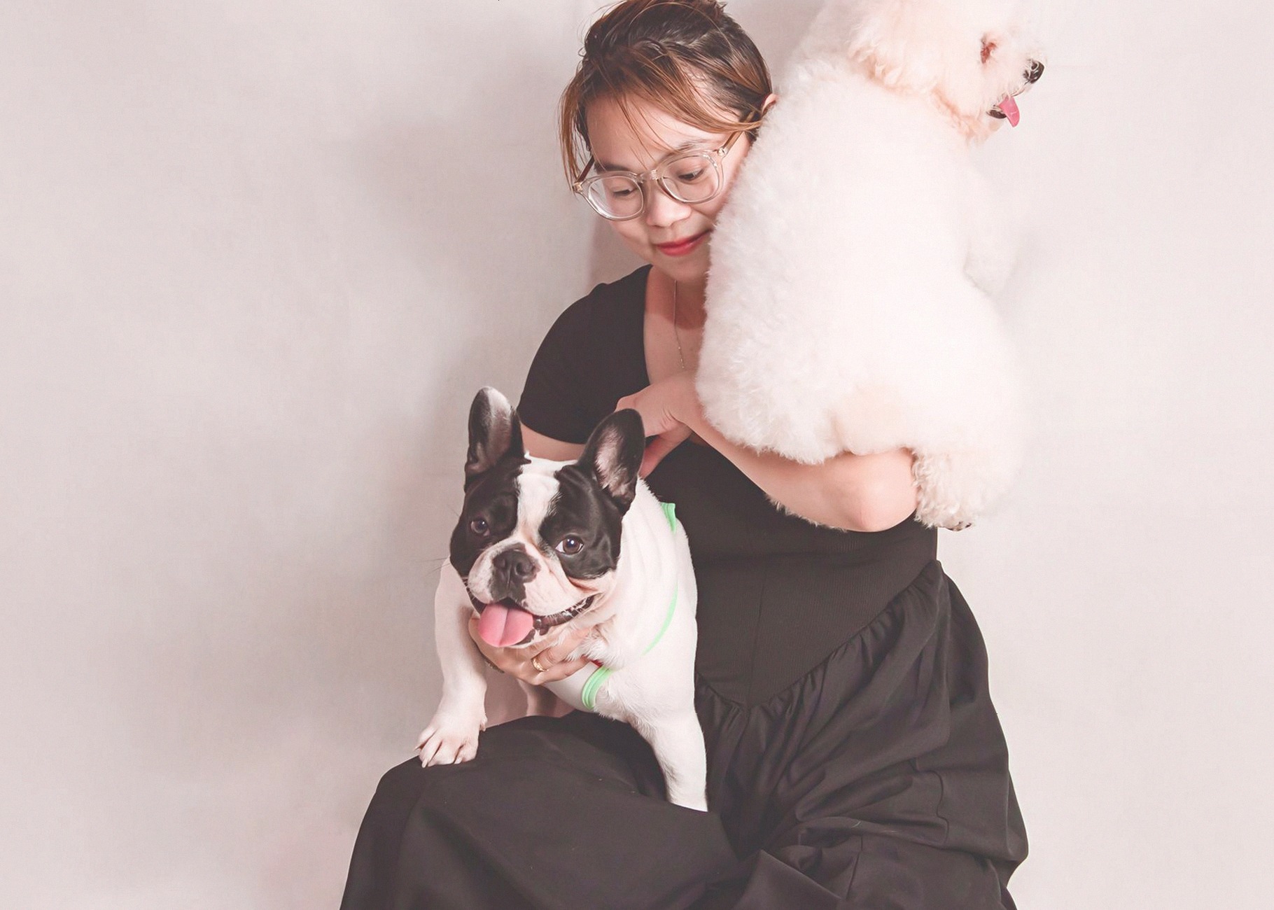 Charming portrait of a woman holding a French Bulldog and a Bolognese dog with a soft backdrop.